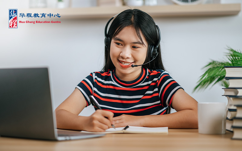 Student with headset attending an online class and taking notes